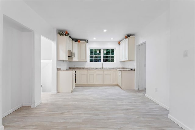 kitchen with light wood-type flooring, ventilation hood, sink, and cream cabinetry