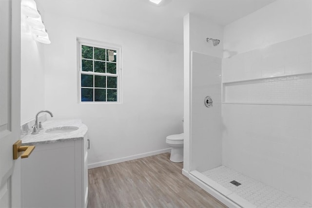 bathroom with tiled shower, hardwood / wood-style floors, vanity, and toilet