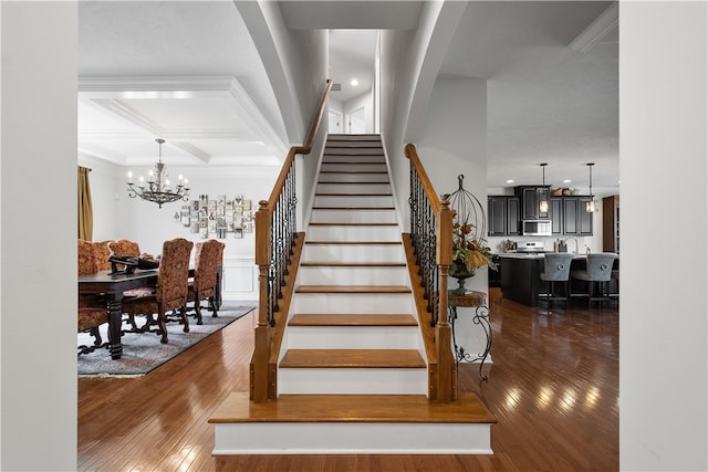 stairway with coffered ceiling, beamed ceiling, an inviting chandelier, and hardwood / wood-style floors