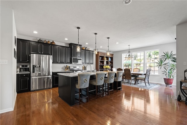 kitchen with an island with sink, hanging light fixtures, stainless steel appliances, a kitchen breakfast bar, and dark hardwood / wood-style flooring