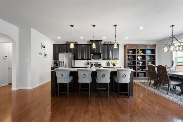 kitchen with decorative light fixtures, an island with sink, stainless steel appliances, and dark hardwood / wood-style flooring