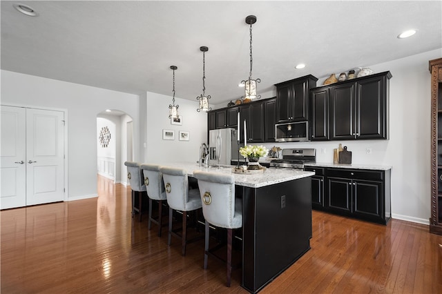 kitchen featuring a kitchen island with sink, a breakfast bar area, dark wood-type flooring, hanging light fixtures, and appliances with stainless steel finishes