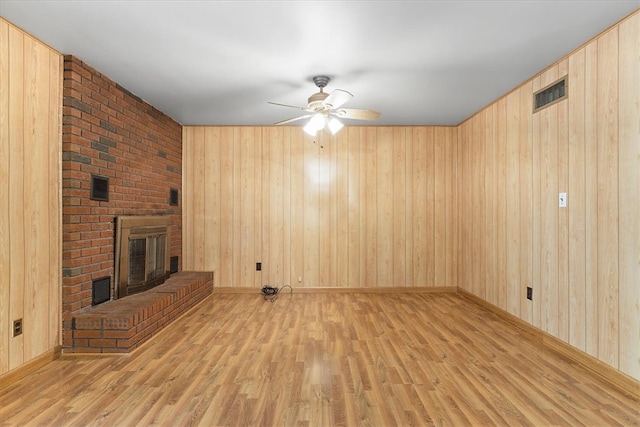 unfurnished living room with wood walls, a brick fireplace, light wood-type flooring, and ceiling fan