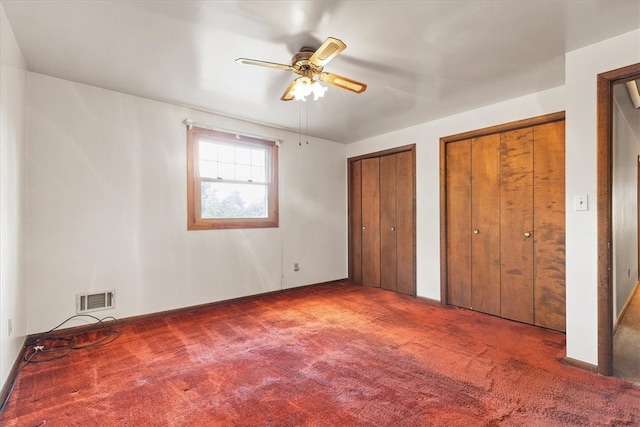 unfurnished bedroom featuring ceiling fan, two closets, and dark carpet