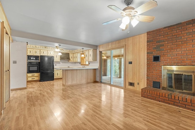 unfurnished living room with wood walls, a brick fireplace, light wood-type flooring, and ceiling fan