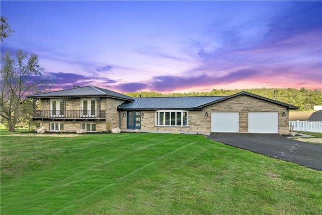 split level home with metal roof, aphalt driveway, an attached garage, a yard, and stone siding