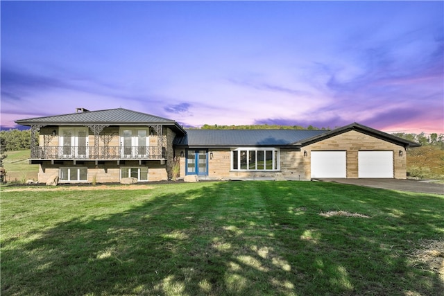 tri-level home with driveway, a garage, metal roof, and a lawn