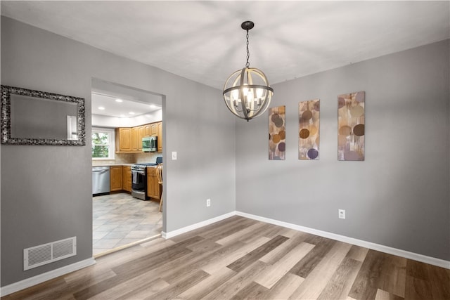 unfurnished dining area featuring an inviting chandelier and light hardwood / wood-style flooring