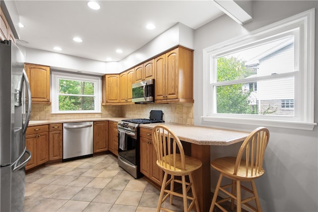 kitchen with light tile patterned floors, appliances with stainless steel finishes, a breakfast bar, and decorative backsplash