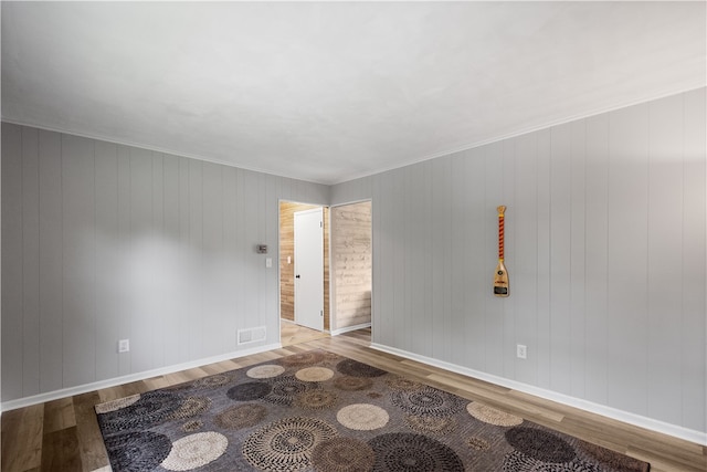 empty room with ornamental molding, hardwood / wood-style floors, and wooden walls