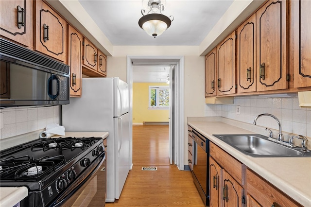 kitchen with light wood-type flooring, black appliances, sink, and tasteful backsplash