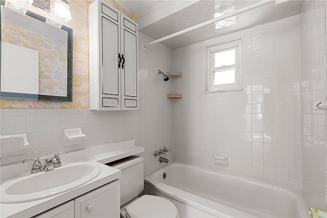 full bathroom featuring tiled shower / bath, vanity, tile walls, and toilet