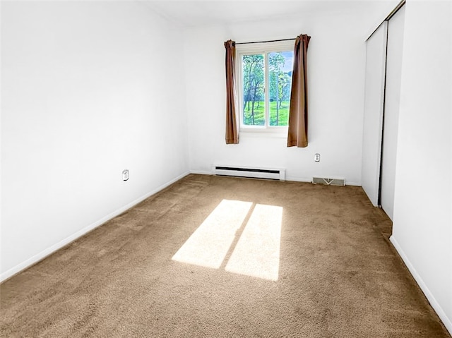 carpeted spare room with a baseboard heating unit