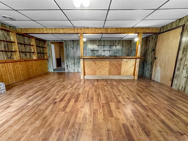 basement featuring bar area, wooden walls, a drop ceiling, and hardwood / wood-style floors