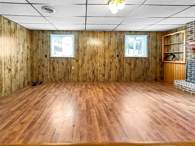 interior space featuring a paneled ceiling, wood-type flooring, a fireplace, and wooden walls