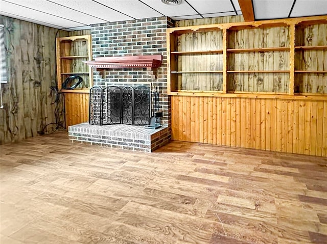 unfurnished living room featuring built in features, a brick fireplace, wooden walls, and hardwood / wood-style flooring