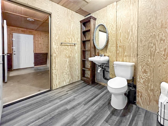 bathroom with wood-type flooring, sink, wooden walls, and toilet