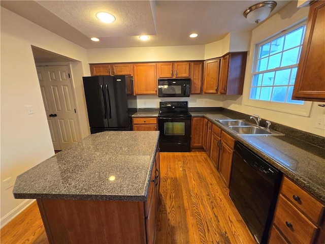 kitchen featuring sink, light hardwood / wood-style flooring, a kitchen island, dark stone counters, and black appliances