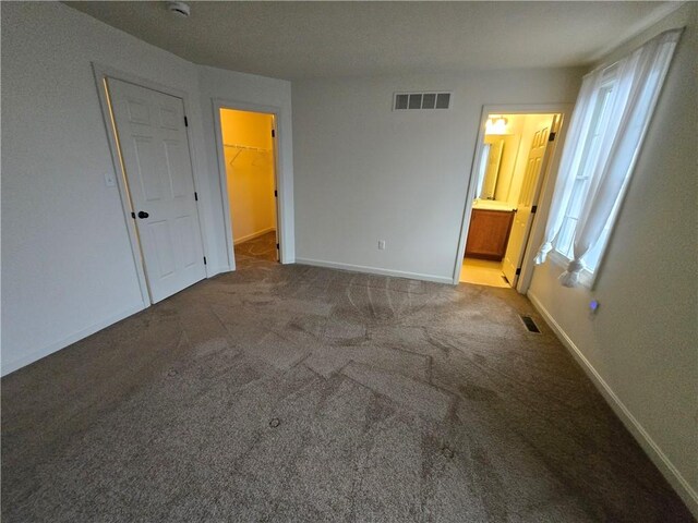 unfurnished bedroom featuring ensuite bathroom, carpet flooring, and a spacious closet