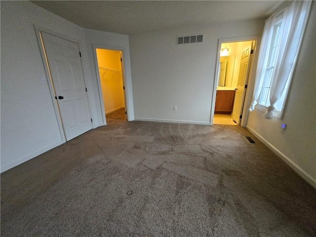 unfurnished bedroom featuring connected bathroom, a walk in closet, and carpet