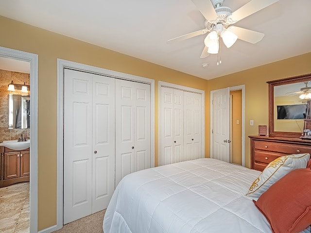 bedroom featuring ceiling fan, multiple closets, ensuite bath, and light carpet