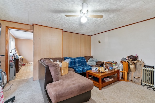 carpeted living room with wooden walls, ceiling fan, radiator, and crown molding