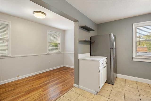 kitchen with stainless steel fridge, light wood-type flooring, and white cabinets