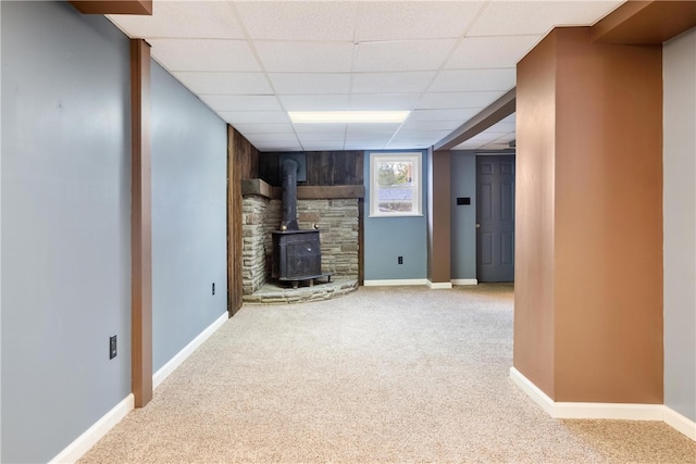 basement featuring a wood stove, a paneled ceiling, and light colored carpet