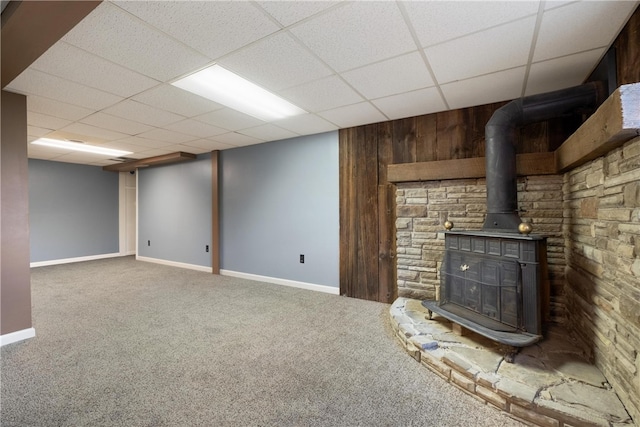 basement with a drop ceiling, a wood stove, and carpet floors