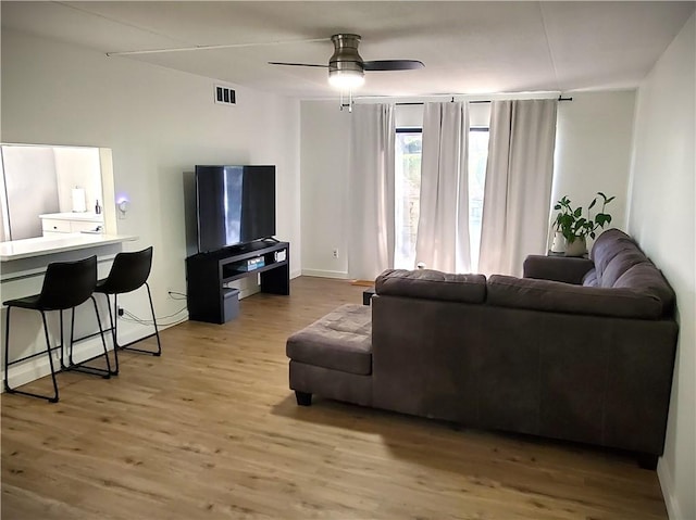 living room featuring visible vents, baseboards, a ceiling fan, and wood finished floors
