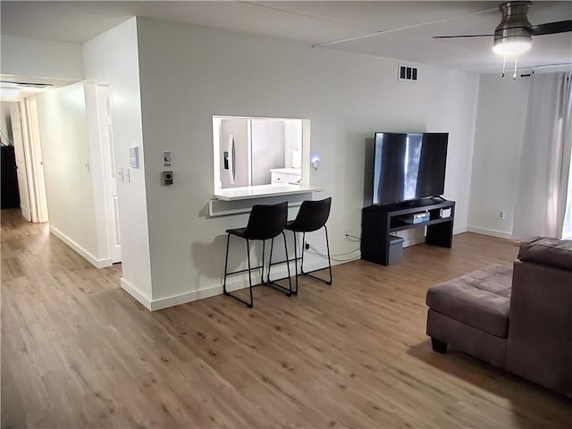 living room featuring wood finished floors, ceiling fan, baseboards, and visible vents