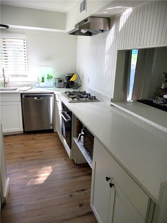 kitchen with light wood-style flooring, white cabinets, under cabinet range hood, appliances with stainless steel finishes, and a sink