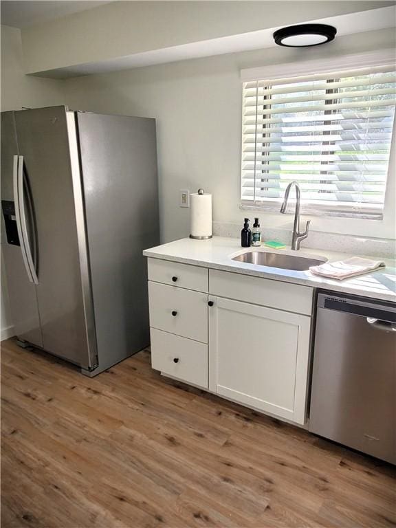 kitchen with white cabinets, a sink, light countertops, light wood-type flooring, and appliances with stainless steel finishes