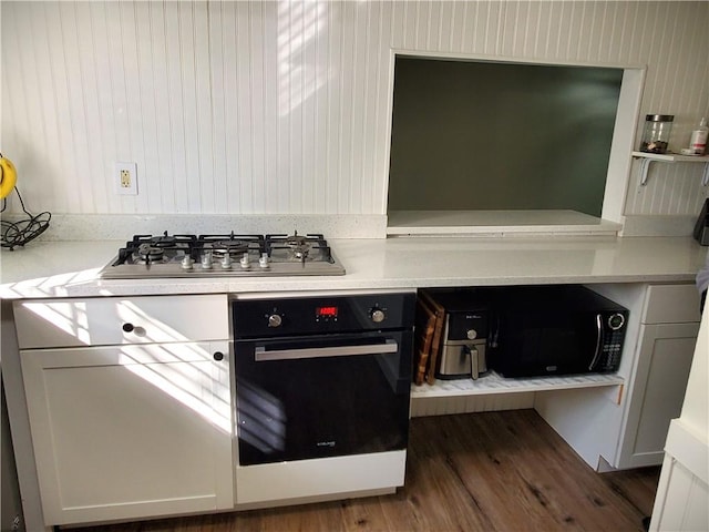 kitchen with dark wood-type flooring, oven, stainless steel gas stovetop, and light countertops