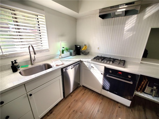 kitchen featuring a sink, under cabinet range hood, light wood finished floors, stainless steel appliances, and light stone counters