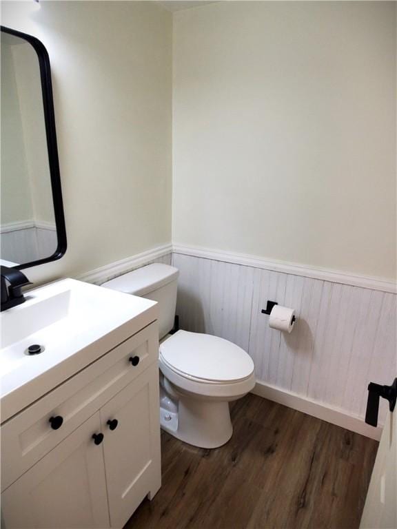 half bath with toilet, wood finished floors, vanity, and a wainscoted wall