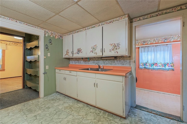 kitchen with a paneled ceiling, white cabinetry, and sink