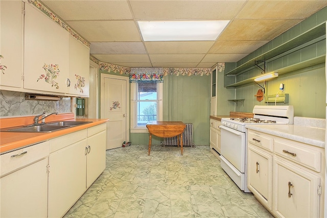 kitchen with a paneled ceiling, radiator heating unit, sink, gas range gas stove, and white cabinetry