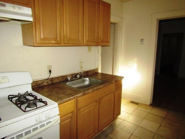 kitchen featuring a sink, under cabinet range hood, white range with gas stovetop, light tile patterned flooring, and dark countertops