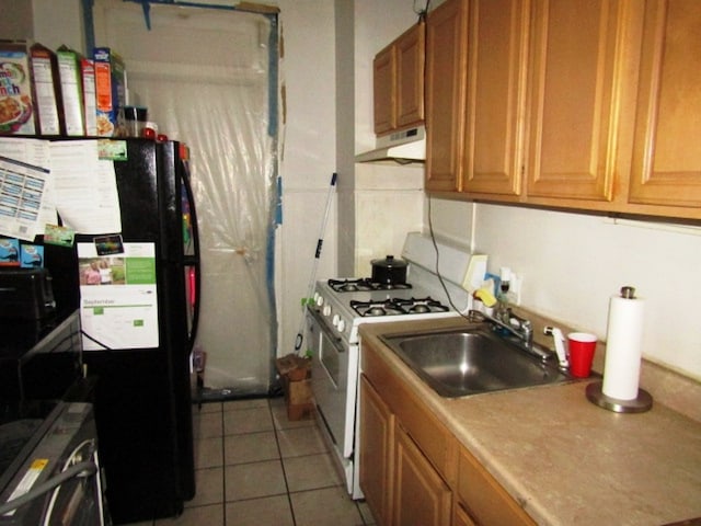 kitchen featuring white gas range oven, black refrigerator, tile patterned flooring, and sink