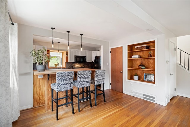 kitchen featuring white cabinetry, a breakfast bar, black appliances, kitchen peninsula, and light hardwood / wood-style flooring