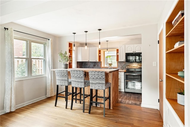 kitchen with light hardwood / wood-style floors, white cabinets, a breakfast bar, kitchen peninsula, and electric range