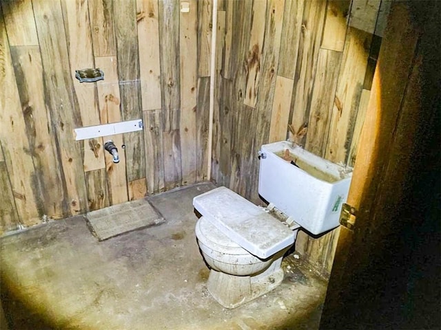 half bath with concrete flooring, wooden walls, and toilet