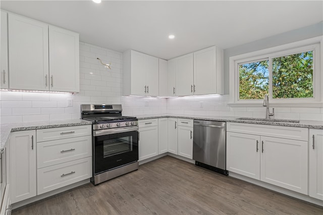 kitchen with stainless steel appliances, white cabinets, hardwood / wood-style flooring, sink, and backsplash