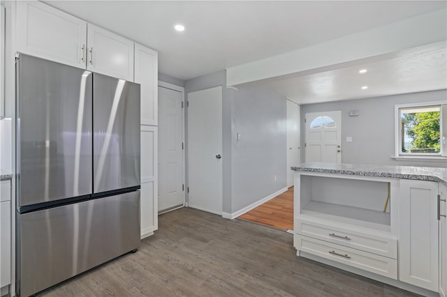 kitchen featuring light stone countertops, stainless steel refrigerator, white cabinets, and hardwood / wood-style floors