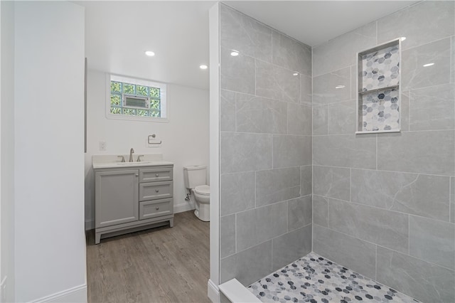 bathroom featuring tiled shower, hardwood / wood-style floors, vanity, and toilet