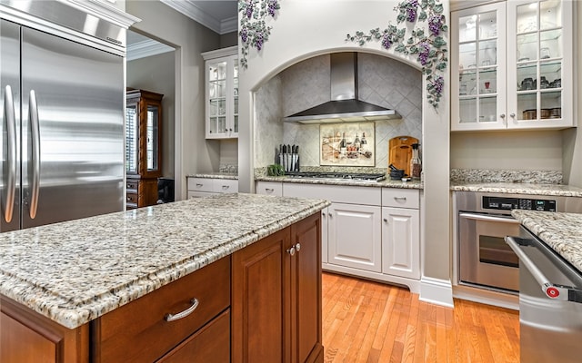 kitchen with light hardwood / wood-style flooring, stainless steel appliances, wall chimney range hood, and white cabinetry