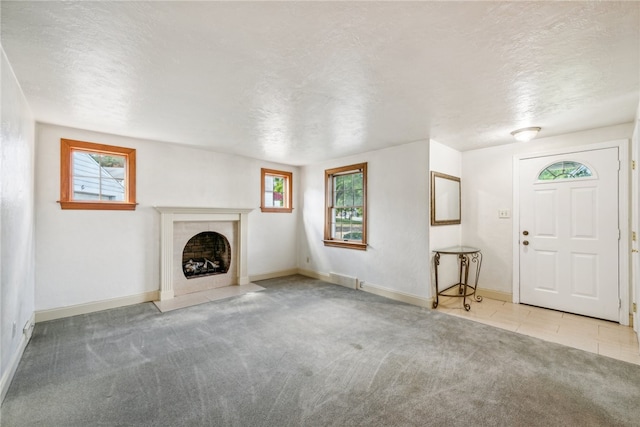 unfurnished living room featuring light carpet, a tile fireplace, and a textured ceiling