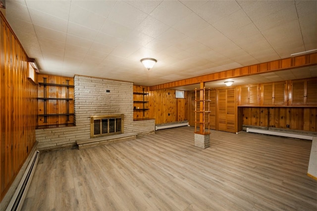 basement featuring wood-type flooring, wooden walls, a fireplace, and a baseboard heating unit