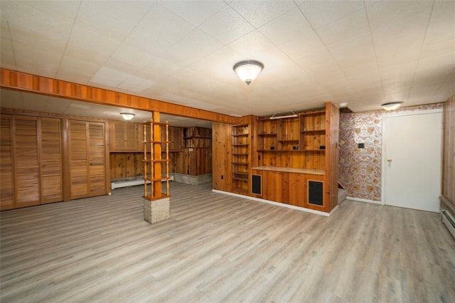 basement with wooden walls, light hardwood / wood-style flooring, and a baseboard heating unit